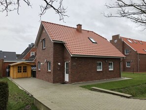 A two-story brick house with a red-tiled roof, a small wooden structure to the left, and a paved driveway. - Fiete - Beautiful vacation home directly in the village center! (Krummhörn)