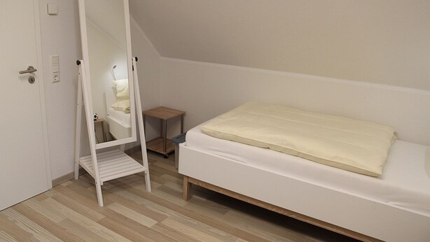 A bedroom with a single bed, a wooden floor, a white door, and a small wooden nightstand. - Fiete - Beautiful vacation home directly in the village center! (Krummhörn)