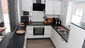 A modern kitchen with white cabinets, a black countertop, a microwave, a stove, and a sink. - Fiete - Beautiful vacation home directly in the village center! (Krummhörn)