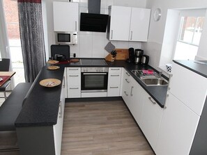 A modern kitchen with white cabinets, a black countertop, a microwave, a stove, and a sink. - Fiete - Beautiful vacation home directly in the village center! (Krummhörn)