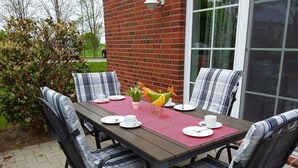 A dining table set outdoors with chairs, a brick wall, and a window in the background. - Fiete - Beautiful vacation home directly in the village center! (Krummhörn)