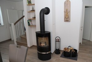 A modern living room with a black wood-burning stove, a leather chair, a bookshelf, and a decorative wooden plaque on the wall. - Fiete - Beautiful vacation home right in the heart of the village! (Krummhörn)