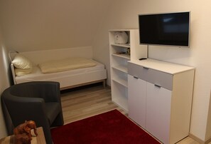 A compact room with a bed, a desk, a chair, a TV, and a red rug. - Fiete - Beautiful vacation home right in the heart of the village! (Krummhörn)