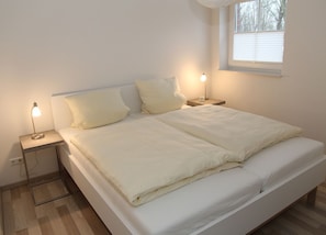 Una cama bien hecha con ropa de cama blanca, dos mesitas de noche con lámparas y una ventana con persianas.