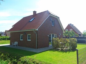 A single-story brick house with a sloped red-tiled roof, a small attached garage, and a well-maintained lawn.