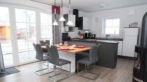 A modern kitchen with a central island, dining table with chairs, and a large window providing natural light. - Fiete - Beautiful vacation home directly in the village center! (Krummhörn)