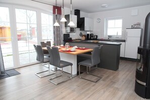 A modern kitchen with a central island, dining table with chairs, and a large window providing natural light. - Fiete - Beautiful vacation home directly in the village center! (Krummhörn)
