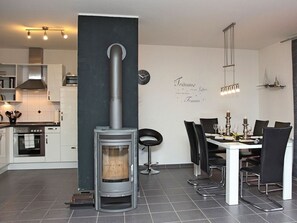 A modern kitchen with a wood-burning stove, a dining area with a white table and black chairs, and a wall-mounted clock.