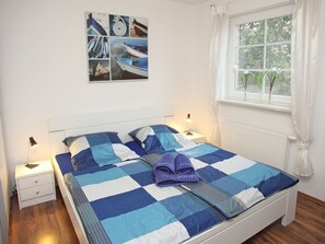 A bedroom with a checkered bedspread, a nightstand with a lamp, a window with curtains, and a wall with a collage of images.