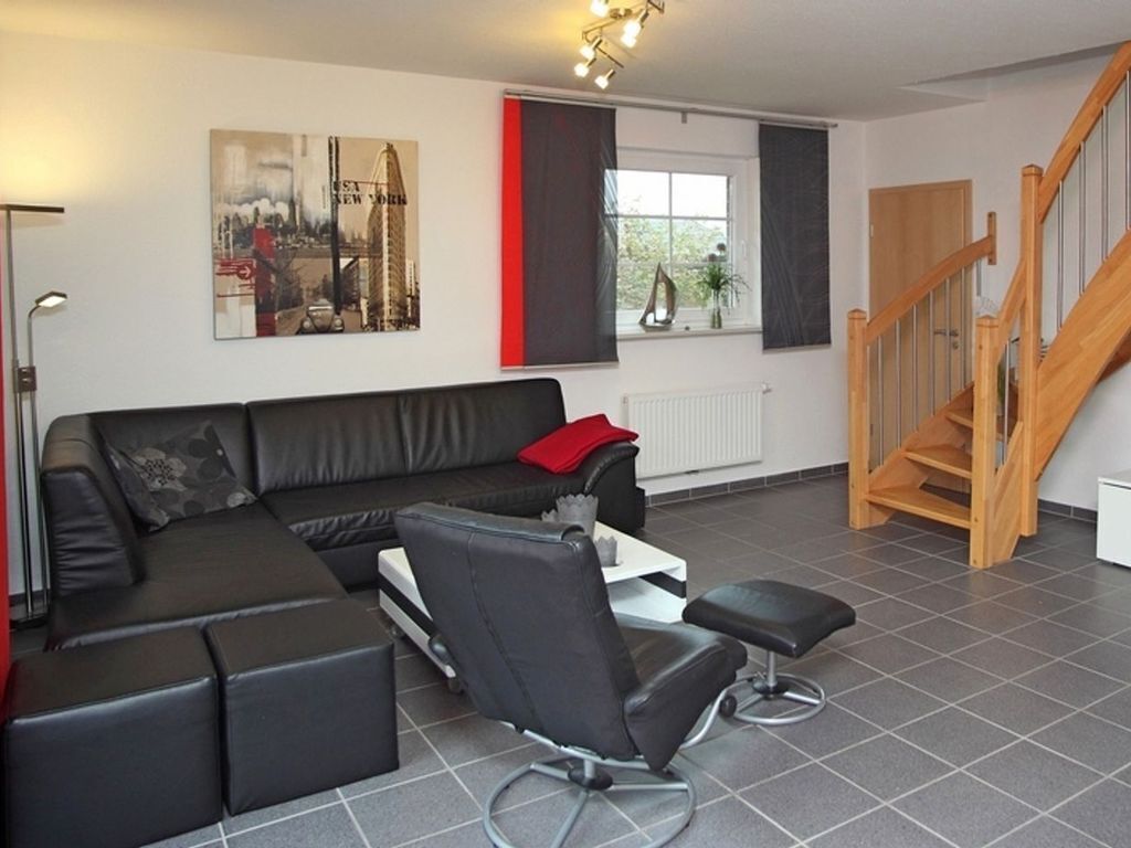 Een moderne woonkamer met een zwarte leren bank, een zwarte fauteuil en een houten trap.