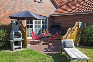 A patio with a grill, red chairs, and a table.