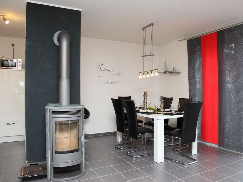 A modern kitchen with a built-in wood stove, a dining area with a white table and black chairs, and a red accent wall.