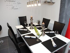 Ein Esstisch, gedeckt mit schwarzen Platzsets, weißen Servietten und Kerzen.