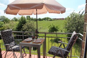 A balcony with a table set for two, a cushioned chair, and a large umbrella.