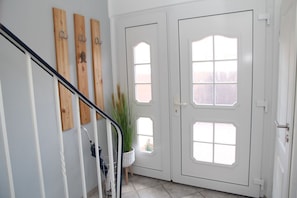 Eine Treppe mit Metallgeländer, Wandverzierungen aus Holz, einem Blumentopf und einer Doppeltür mit Glasscheiben.