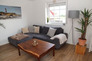 Una sala de estar con un sofá seccional gris, una mesa de centro de madera, una planta en maceta y un cuadro de un faro.