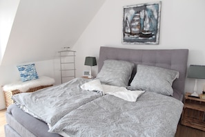Ein Schlafzimmer mit einem Bett, einem Nachttisch, einer Lampe, einer Wanduhr, einer Leiter und einem Gemälde.