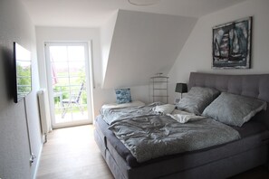 A bedroom with a large bed, a nightstand, a lamp, and a painting on the wall.
