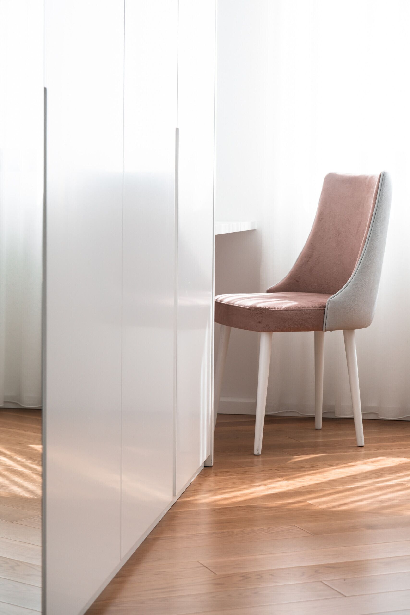 A modern room with a wooden floor, a white wardrobe, and a pink chair.