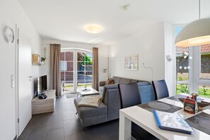 Ein modernes Wohnzimmer mit einer Couch, einem Esstisch und einem Fernseher.