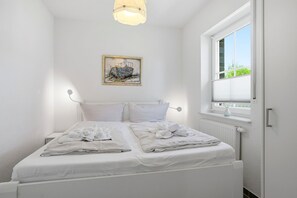 Ein helles Schlafzimmer mit Bett, Nachttisch, Fenster mit Jalousien und einer Wandleuchte.