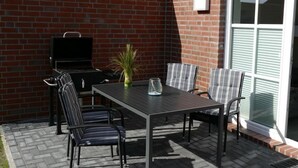 Een terras met een bakstenen muur, een barbecue, een tafel met stoelen en een bloempot.