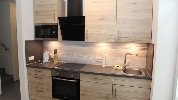 Een kleine keuken met houten kastjes, een ingebouwde magnetron, een roestvrijstalen spoelbak en een broodrooster.