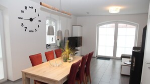 Een moderne eetruimte met een houten tafel, rode stoelen en een wandklok.