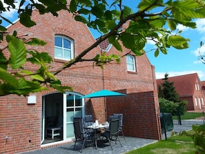 A brick house with a patio area featuring a table and chairs under a blue umbrella. - Anchorage - Family-friendly semi-detached house in a quiet location (Krummhörn)