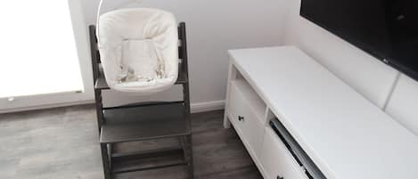 Une pièce comprenant un meuble de rangement blanc pour appareils multimédias, un fauteuil noir et un grand téléviseur à écran plat.