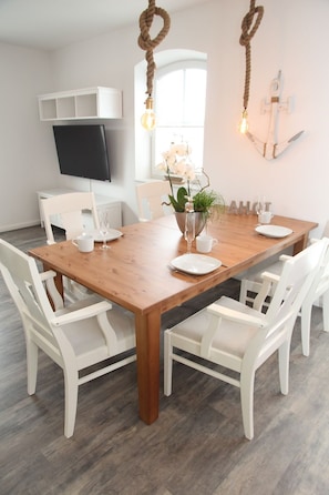 A dining area with a wooden table and white chairs, a potted plant, and a mounted television.