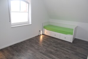 Una habitación pequeña con una cama individual, una ventana y suelo de madera.