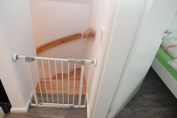 A white baby gate installed at the top of a wooden staircase.