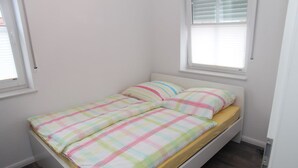 A small, single-bed room with a plain white wall, a window with blinds, and a wooden floor. - Anchorage - Family-friendly semi-detached house in a quiet location (Krummhörn)