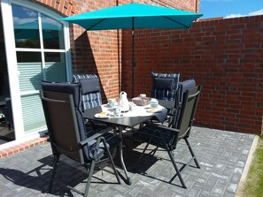 A patio with a table and four chairs, an umbrella, and a brick wall.