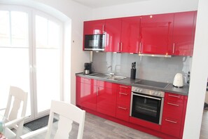 A modern kitchen with red cabinets, a stainless steel oven, and a black microwave.