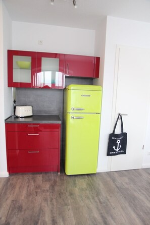 Una cucina compatta con mobili rossi, un frigorifero giallo e una porta bianca.