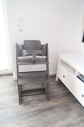 A room with a grey multi-tiered storage unit, a white desk with drawers, and a light-colored wooden floor.