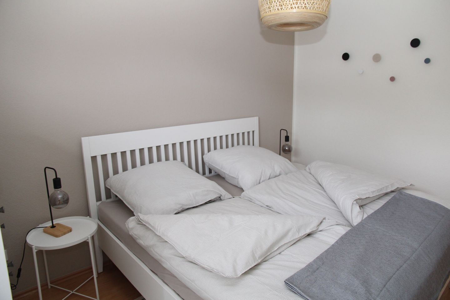 A neatly made bed with white bedding, a small bedside table with a lamp, and a wall-mounted light fixture.