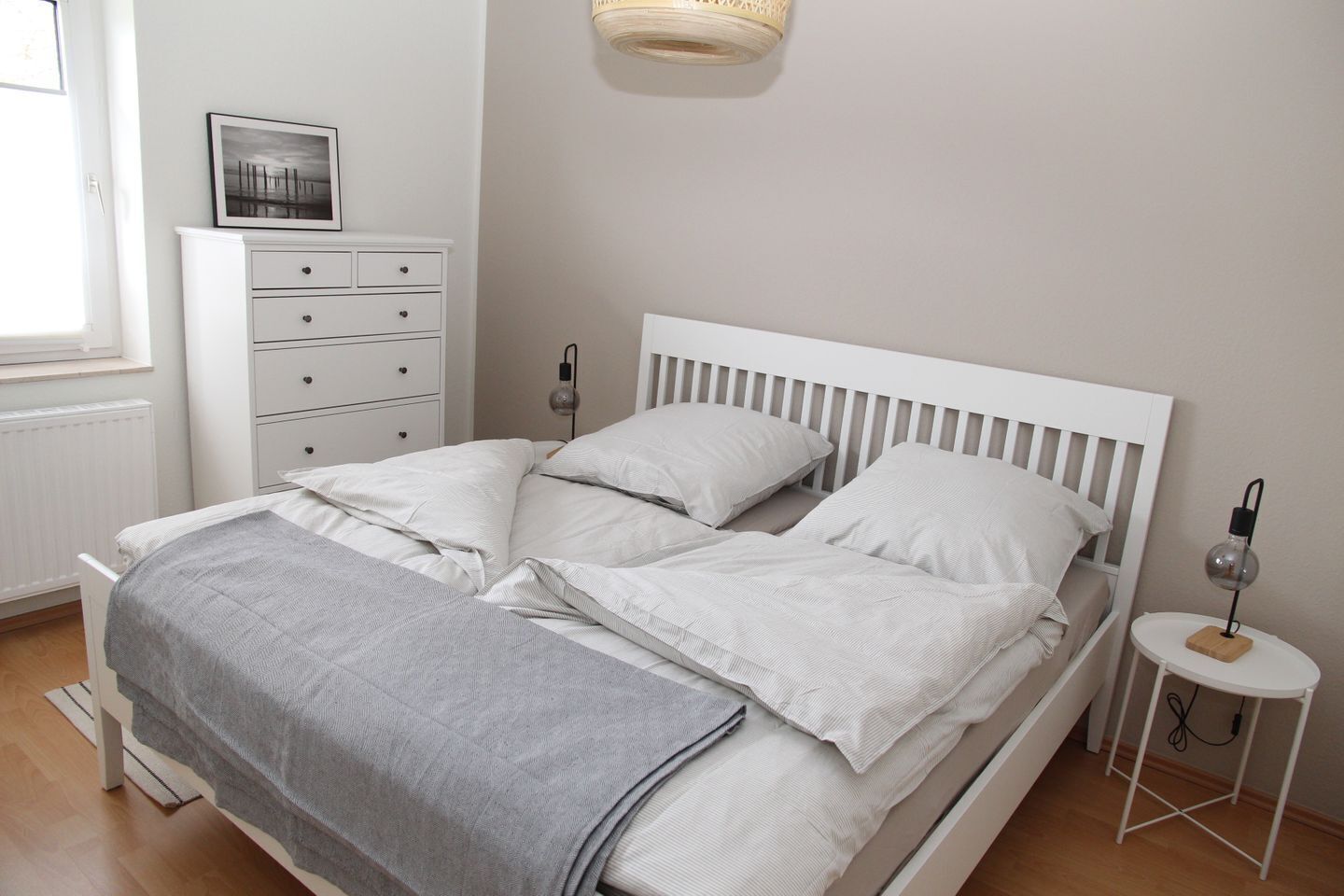 A neatly made bed with white bedding, a bedside table with a lamp, and a dresser with drawers.