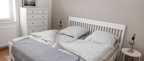 A neatly made bed with white bedding, a bedside table with a lamp, and a dresser with drawers.