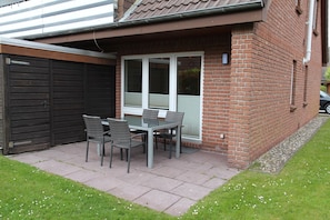 A patio with a table and chairs, a garage door, and a brick house. - Biene - Cozy, newly renovated vacation apartment for 3 people (Krummhörn)