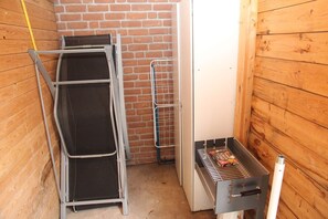 Une petite pièce fermée, avec un mur en briques, une échelle en métal, un gril et une étagère en métal.