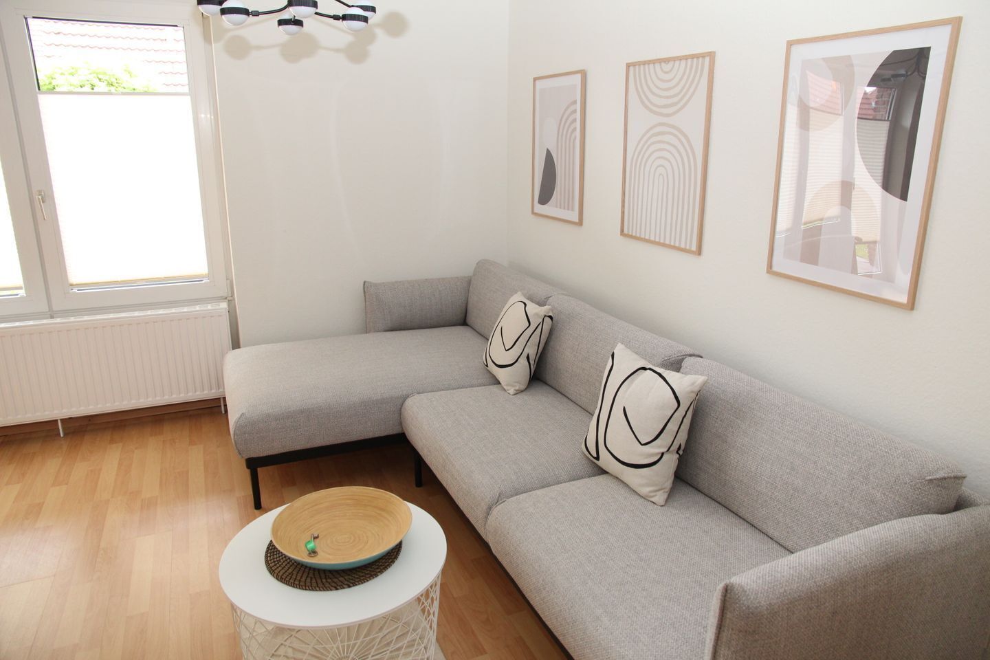 A modern living room with a grey sectional sofa, two decorative pillows, a round coffee table, and three framed artworks on the wall.