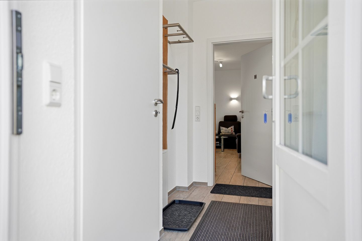 Een gang met een deur naar een kamer, een handdoekrek, een stoel en een douche.