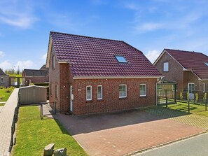 A two-story brick house with a red-tiled roof, a small attached garage, and a paved driveway. - Nordseeperle - 100sqm vacation home for 6 people + dog with fireplace, sauna & garden (Krummhörn)
