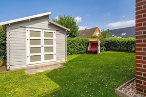 A small, single-story shed with a white exterior and a garage door, surrounded by a well-maintained lawn and a red chair. - Gode Stuuv - Our "good room" (75sqm) for 4 persons centrally located in Greetsiel (Krummhörn)