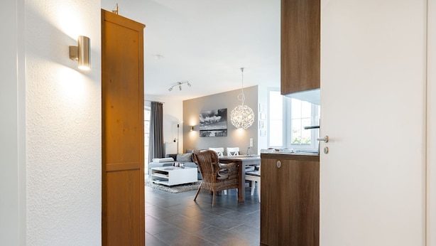 A modern kitchen with dark tiles, wooden cabinets, and a dining area with a white table and wicker chairs. - Gode Stuuv - Our "good room" (75sqm) for 4 persons centrally located in Greetsiel (Krummhörn)