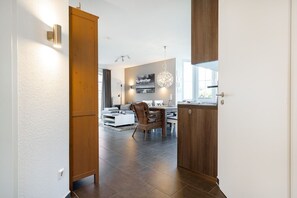 A modern kitchen with dark tiles, wooden cabinets, and a dining area with a white table and wicker chairs. - Stuuv Cottage - Our "nice place" (75 m²), accommodating 4 people, located in the center of Greetsiel (Krummhörn)