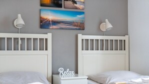 A bedroom with two beds, a nightstand, and wall-mounted lamps. - Gode Stuuv - Our "good room" (75sqm) for 4 persons centrally located in Greetsiel (Krummhörn)